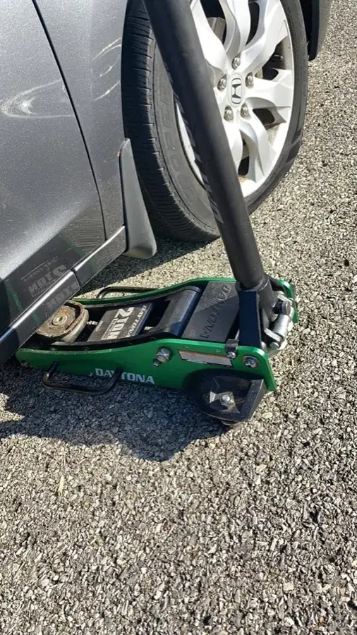 Hydraulic floor jack under a vehicle during a Free The Key roadside tire change